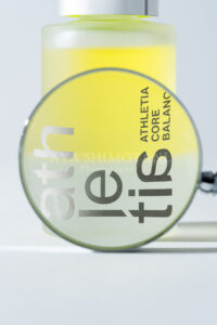 虫眼鏡の歪みを活かしてロゴと2層オイルの境界線を大胆に捉えた、グラフィカルなスキンケア商品広告撮影事例。アイキャッチの強いビジュアル訴求