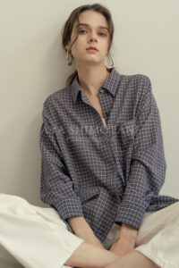 大阪のアパレル撮影スタジオ写真。チェック柄シャツを着たモデルがベッド脇に座るリラックスした雰囲気のカット